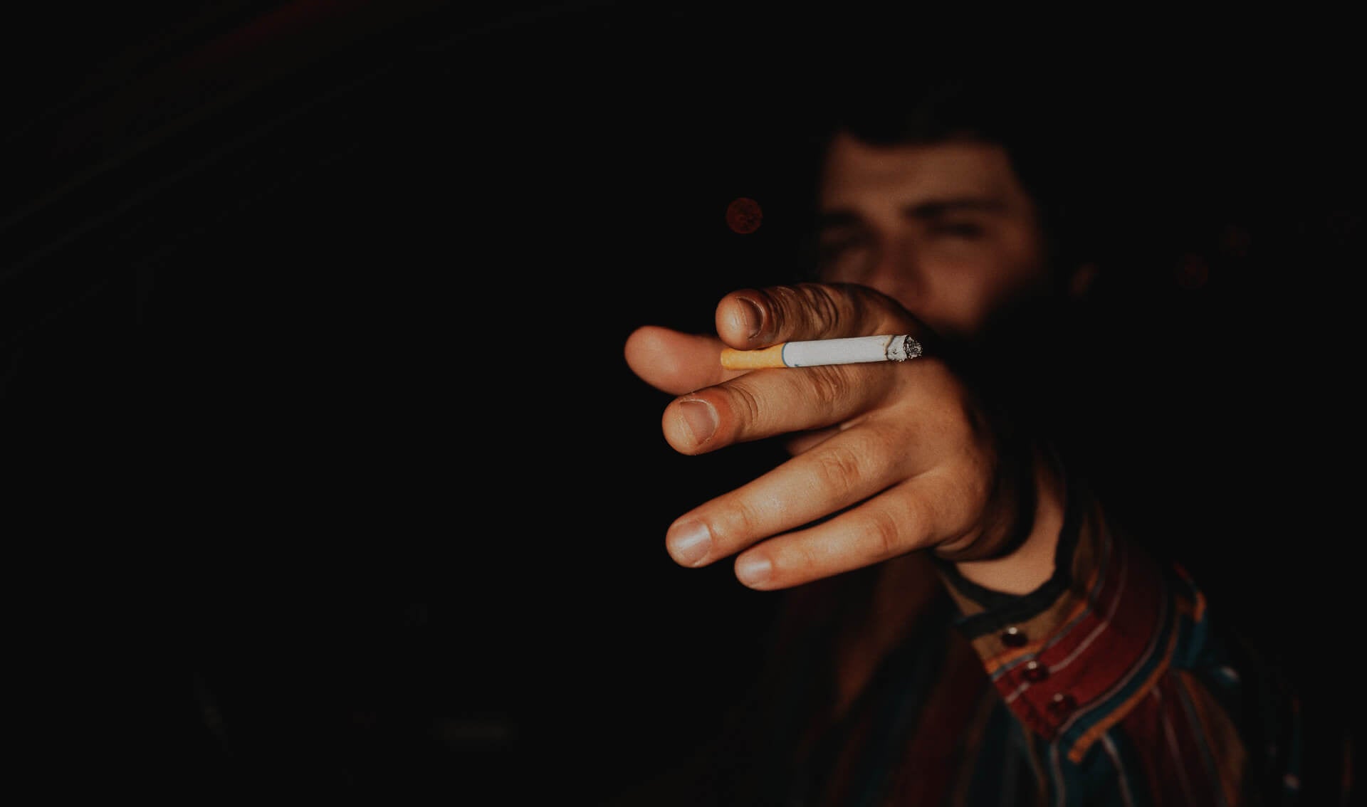 Photo of Gavin in a car with a cigarette pointing at the camera